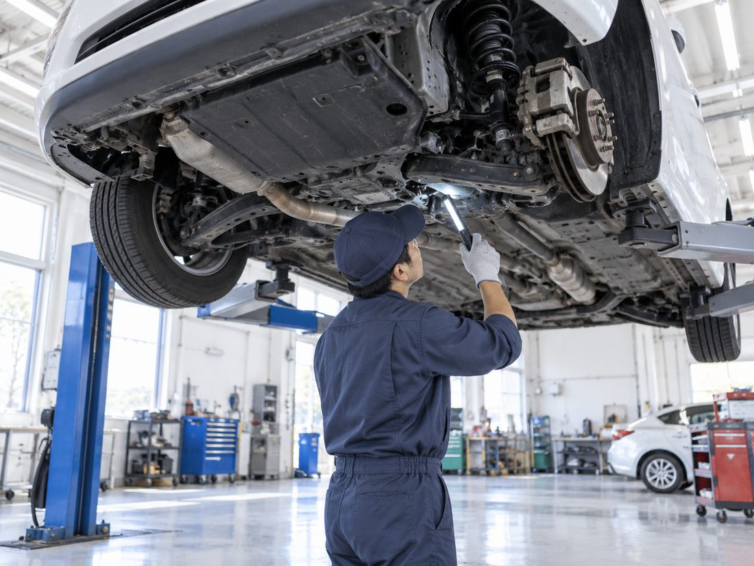 リフトで持ち上げた車の下回りを点検する整備士